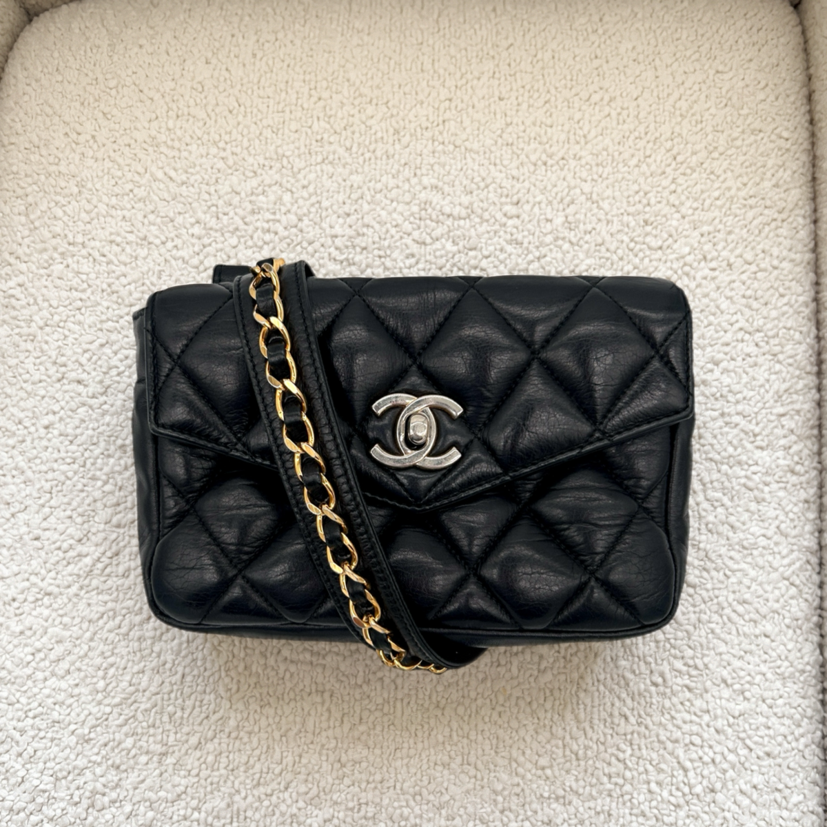 Vintage black Chanel Turnlock belt bag styled on a couch, overhead view